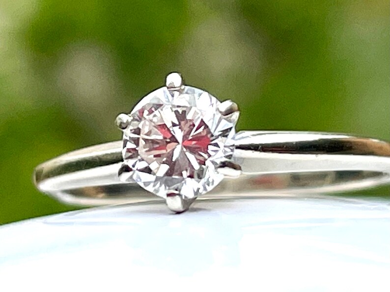 Puede incluir: Un anillo de plata con un diamante transparente redondo y facetado.