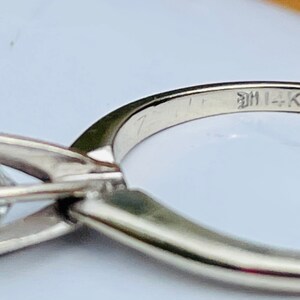 Puede incluir: Un anillo de plata con un solo diamante engastado en garras. La banda est&aacute; inscrita con el texto "14K".