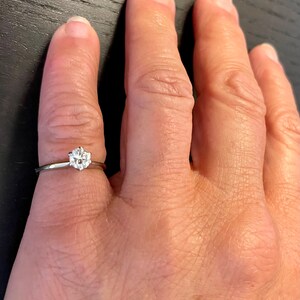 Puede incluir: Un anillo de plata con un solo diamante redondo en el centro.