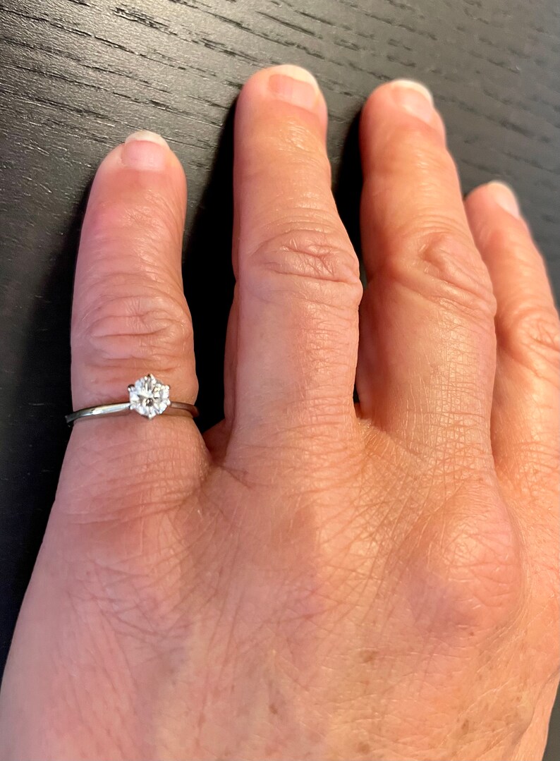 Puede incluir: Un anillo de plata con un solo diamante redondo en el centro.