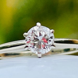 Puede incluir: Un anillo de plata con un solo diamante redondo y transparente.