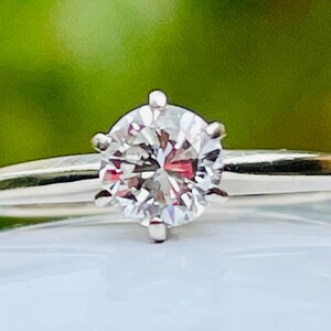 Puede incluir: Un anillo de plata con un diamante redondo y transparente.