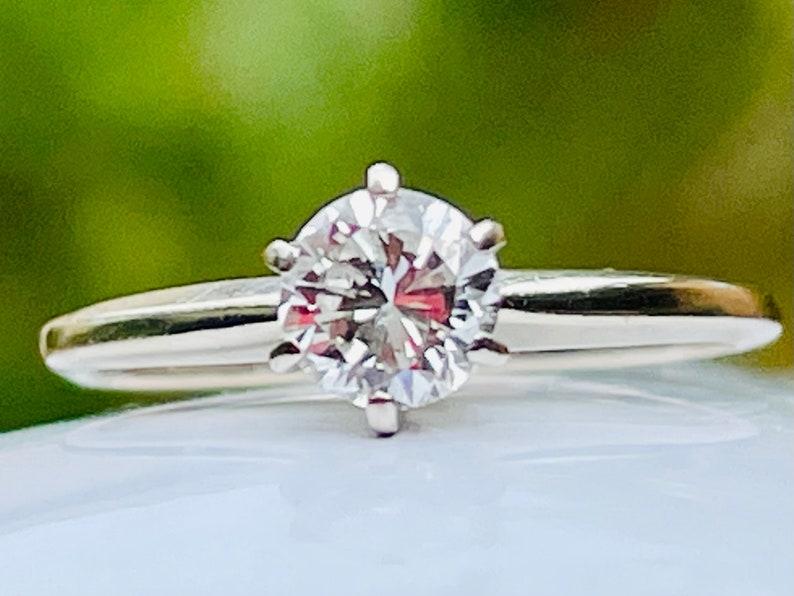 Puede incluir: Un anillo de plata con un diamante redondo y transparente.