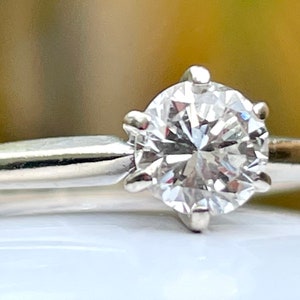 Puede incluir: Un anillo de compromiso solitario de plata con un diamante redondo brillante.