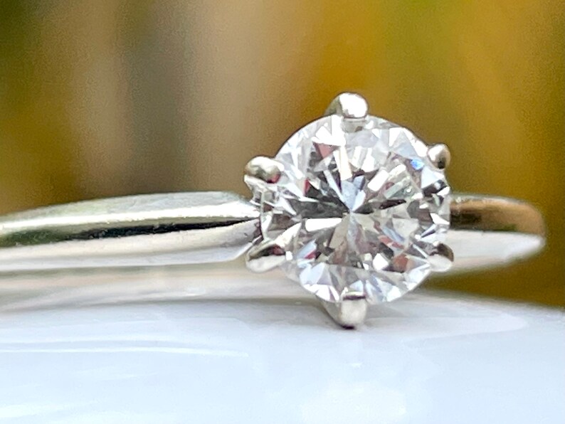 Puede incluir: Un anillo de compromiso solitario de plata con un diamante redondo brillante.