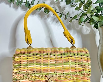 May include: A vintage woven handbag in pastel colors of yellow, green, and peach. The rectangular bag has a yellow handle and a gold-colored clasp. The bag is made of woven wicker and is a retro style.