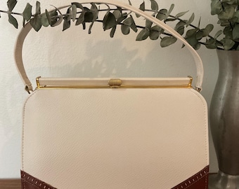 May include: A white and brown leather handbag with a gold clasp and a top handle. The bag has a scalloped bottom edge.