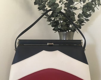 May include: A vintage handbag with a navy blue, white, and red color scheme. The bag has a top handle and a clasp closure.