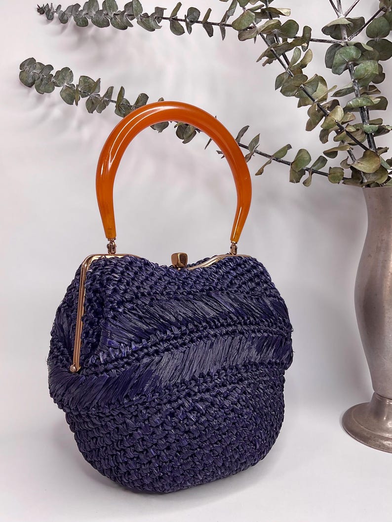 May include: A vintage navy blue woven handbag with a curved amber handle. The bag has a gold-colored clasp and trim. The woven texture creates a unique pattern. The bag is a stylish accessory.