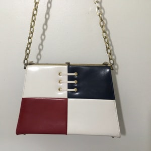 May include: A vintage handbag with a gold chain strap. The bag is made of leather and has a checkered pattern in red, white, and blue.