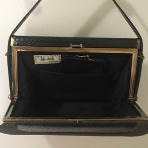 May include: A black leather purse with a gold frame and a small pocket inside. The purse has a short strap and the words "Life Stride" are printed on a label inside.