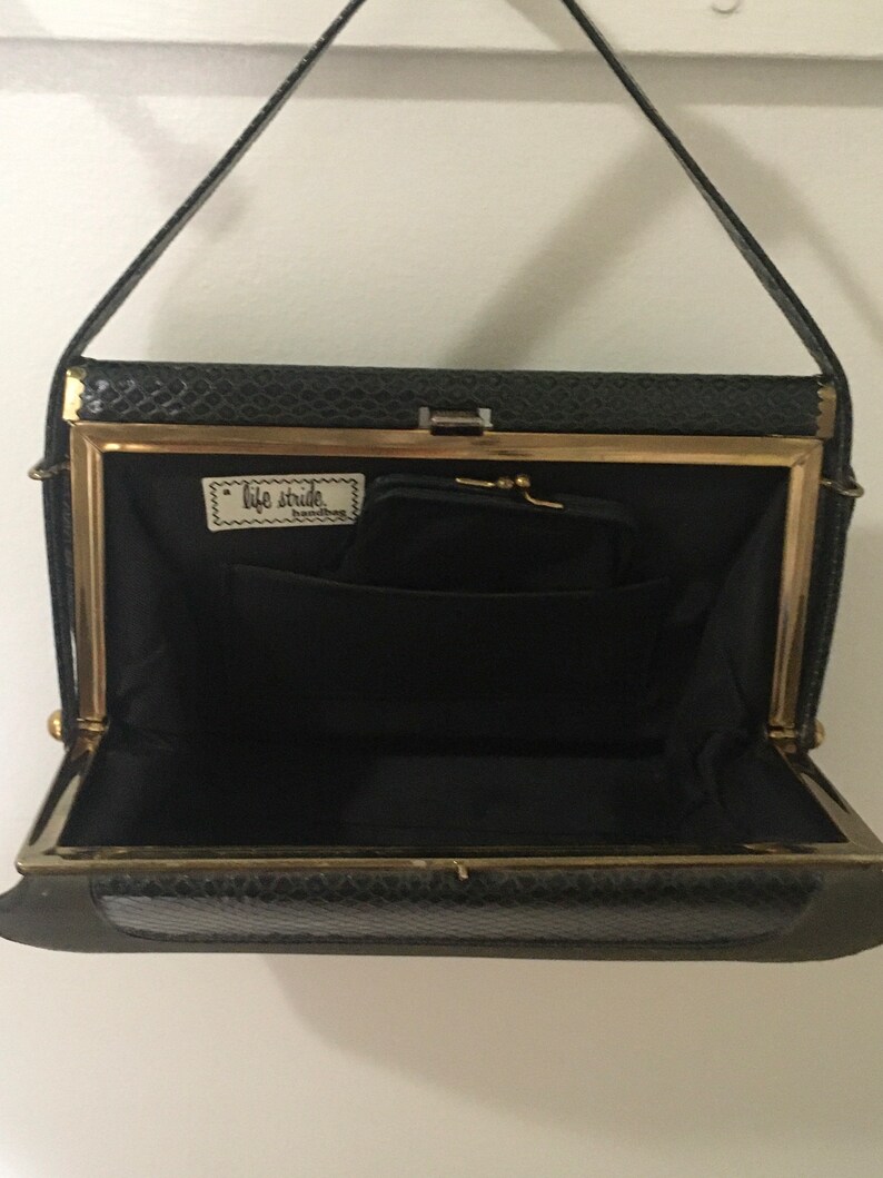 May include: A black leather purse with a gold frame and a small pocket inside. The purse has a short strap and the words "Life Stride" are printed on a label inside.