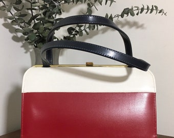 May include: A vintage handbag with a red, white, and blue striped design. The bag has a black leather handle and a gold clasp.
