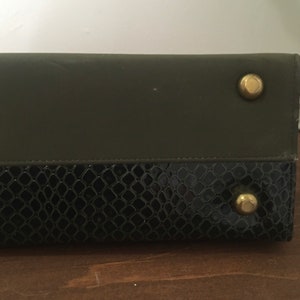 May include: A black and green leather clutch with gold-toned hardware. The clutch has a snakeskin pattern on the bottom half.