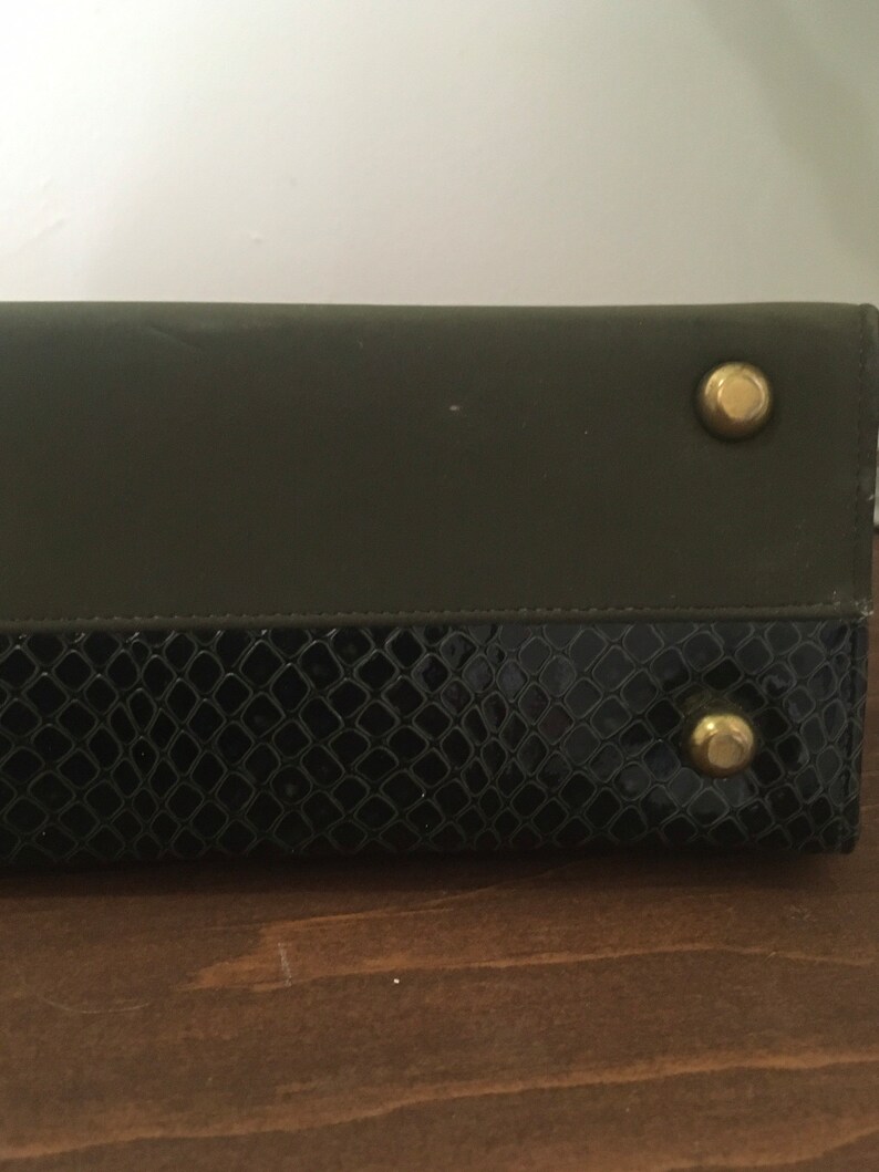May include: A black and green leather clutch with gold-toned hardware. The clutch has a snakeskin pattern on the bottom half.