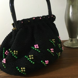 May include: A black crocheted handbag with a black handle and pink and green floral bead embellishments.