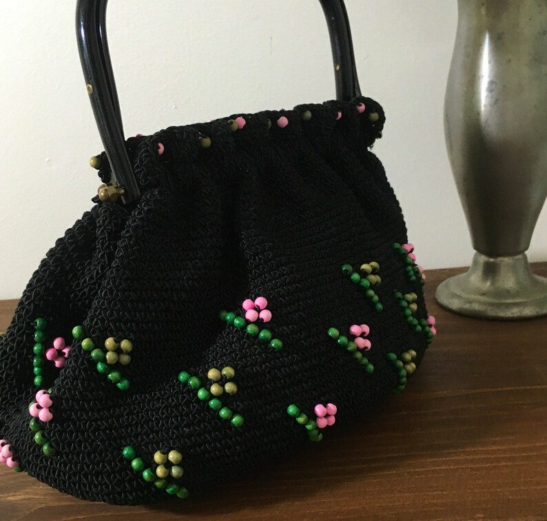 May include: A black crocheted handbag with a black handle and pink and green floral bead embellishments.