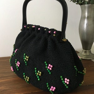 May include: A black beaded handbag with a black woven fabric body and a black plastic handle. The bag is decorated with pink and green beads in a floral pattern.