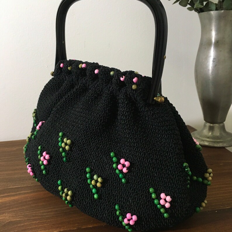 May include: A black beaded handbag with a black woven fabric body and a black plastic handle. The bag is decorated with pink and green beads in a floral pattern.