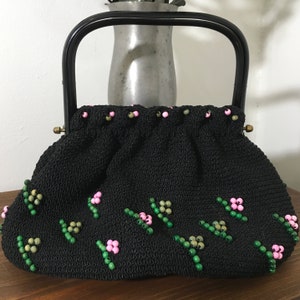 May include: A black crocheted handbag with a black handle and floral bead embellishments in pink and green.