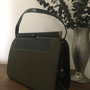 May include: A vintage green and black handbag with a top handle and a clasp closure. The bag has a textured black leather flap and a smooth green fabric body.
