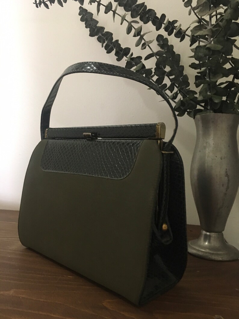 May include: A vintage green and black handbag with a top handle and a clasp closure. The bag has a textured black leather flap and a smooth green fabric body.