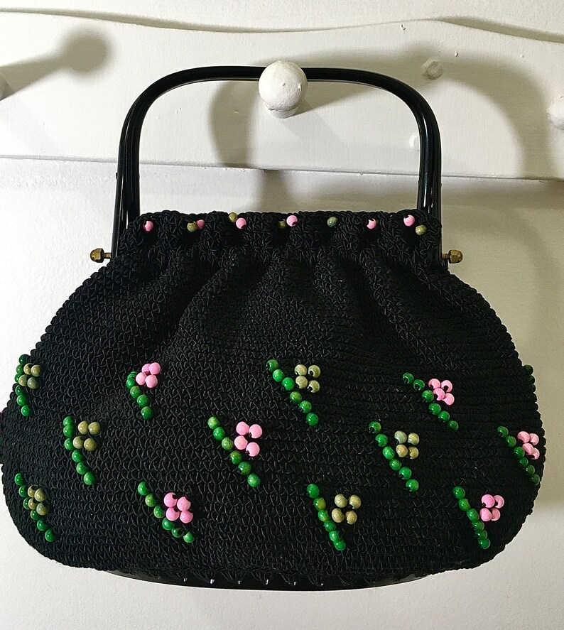 May include: A black crocheted handbag with a black handle and pink and green beaded embellishments.