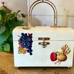 May include: A white vintage box purse with a gold handle and a latch closure. The purse is decorated with a grape cluster, a beet, and a turnip.