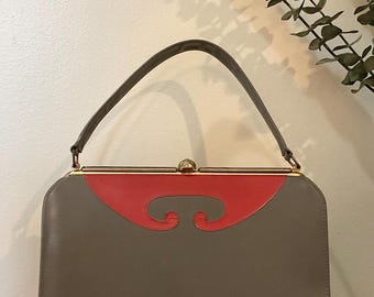 May include: A gray leather handbag with a red leather flap and a gold clasp. The handbag has a single top handle.