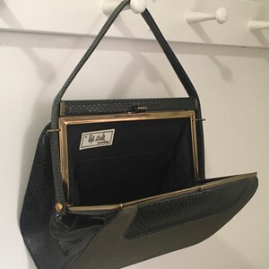 May include: A black and green snakeskin clutch purse with a gold clasp and a label that reads "Tote Studio" inside. The purse is open and hanging from a hook.
