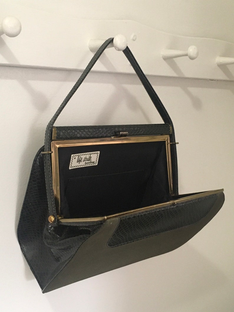 May include: A black and green snakeskin clutch purse with a gold clasp and a label that reads "Tote Studio" inside. The purse is open and hanging from a hook.