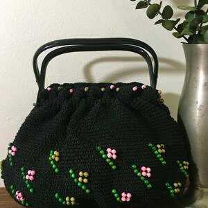 May include: A black crocheted handbag with a black top handle. The bag is decorated with pink and green beads in a floral pattern.