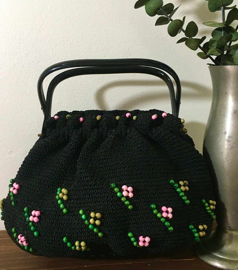 May include: A black crocheted handbag with a black top handle. The bag is decorated with pink and green beads in a floral pattern.