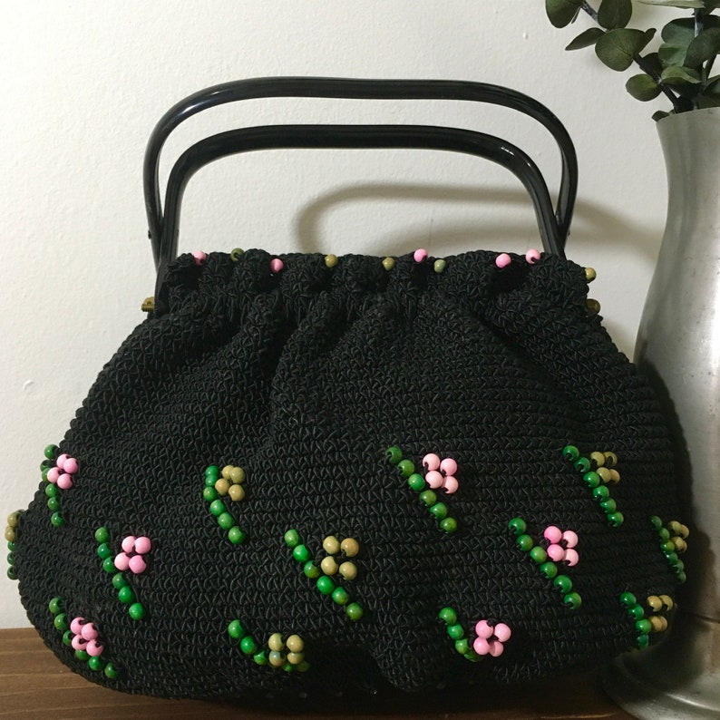 May include: A black crocheted handbag with a black handle and pink and green beaded floral embellishments.