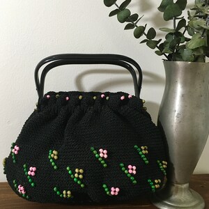 May include: A black crocheted handbag with a black handle and pink and green bead embellishments.