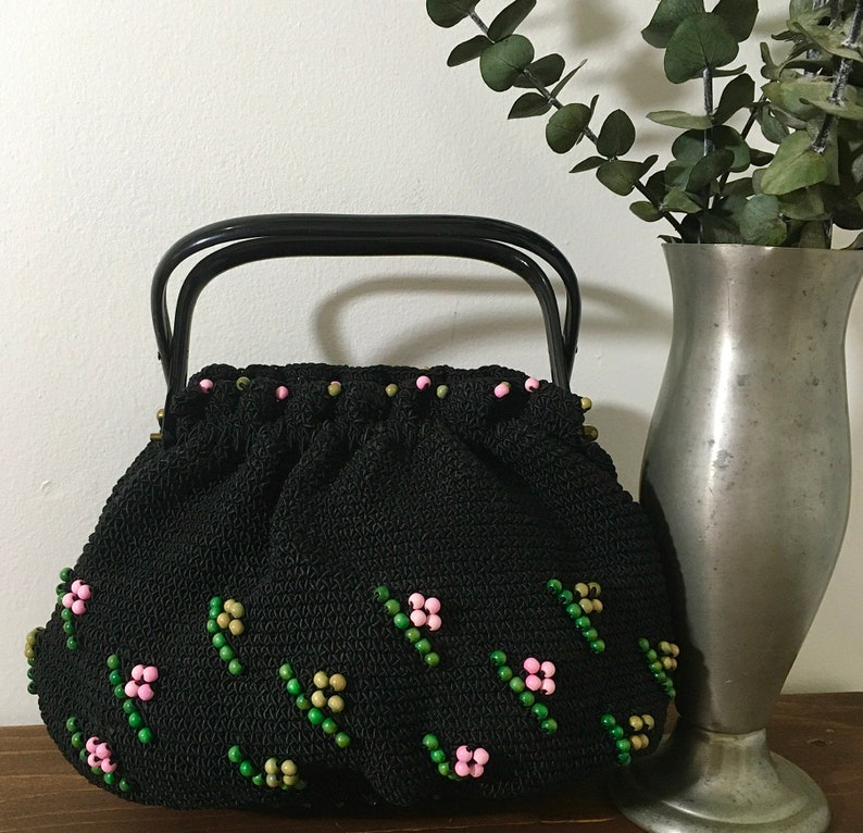 May include: A black crocheted handbag with a black handle and pink and green bead embellishments.
