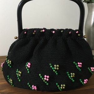 May include: A black crocheted handbag with a black handle and pink and green beaded embellishments.