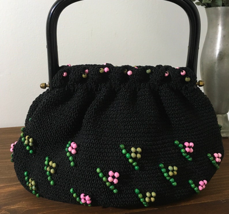 May include: A black crocheted handbag with a black handle and pink and green beaded embellishments.