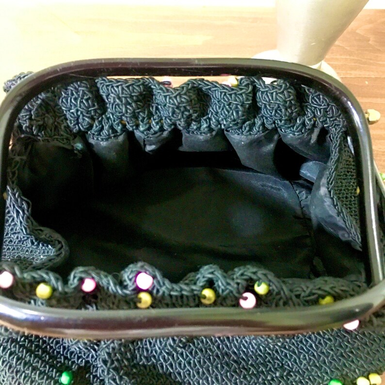 May include: A black crocheted purse with a black plastic frame and gold and pink beads around the edge.