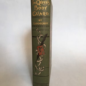 May include: A vintage book titled "The Queen's Body Guard" by Vandegrift. The book's spine is a muted green with gold lettering. A decorative illustration of a quill, ribbon, and a red emblem adorns the spine. The book is published by Henry T. Coates & Co.