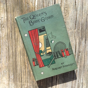 May include: Vintage book titled "The Queen's Body Guard" by Margaret Vandegrift. The book cover is a muted green with illustrations of a tennis racket, books, and a window with a red curtain. The book is resting on a weathered wooden surface.