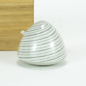 Puede incluir: Una taza de cerámica blanca con asa negra y el texto "But First, Coffee" en negrita negra. La taza se encuentra sobre un fondo borroso, sugiriendo un ambiente acogedor.