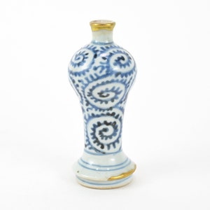 May include: A small, white ceramic vase with a blue and white swirl design. The vase has a gold rim and a rounded base.