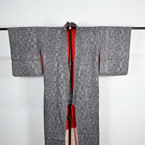 Puede incluir: Un kimono con estampado gris y negro con forro rojo y rosa. El kimono está colgado en un soporte negro.