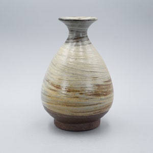 May include: A small, white ceramic vase with brown and beige swirling patterns. The vase has a narrow neck and a rounded body.