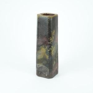 May include: A tall, rectangular vase with a textured surface. The vase has a dark color scheme with shades of brown, purple, and gold. The vase has a square opening at the top.