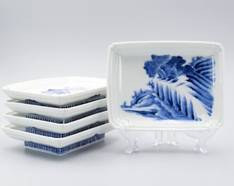 May include: A set of six white square ceramic plates with blue and white floral designs. The plates are stacked on top of each other and are displayed on a white background.