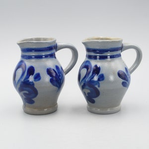 Puede incluir: Dos jarras pequeñas de cerámica azul y blanca con diseños florales. Las jarras tienen un cuerpo redondeado y un asa.