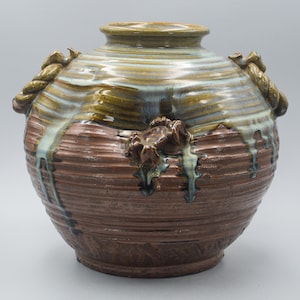 May include: A brown ceramic vase with a green and blue glaze. The vase has rope-like handles and a raised crab design.