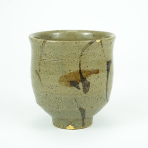 May include: A handcrafted, olive-green ceramic teacup with a unique, irregular shape. The cup features visible repairs with gold accents, showcasing the Japanese art of Kintsugi. The cup is approximately 4 inches tall.